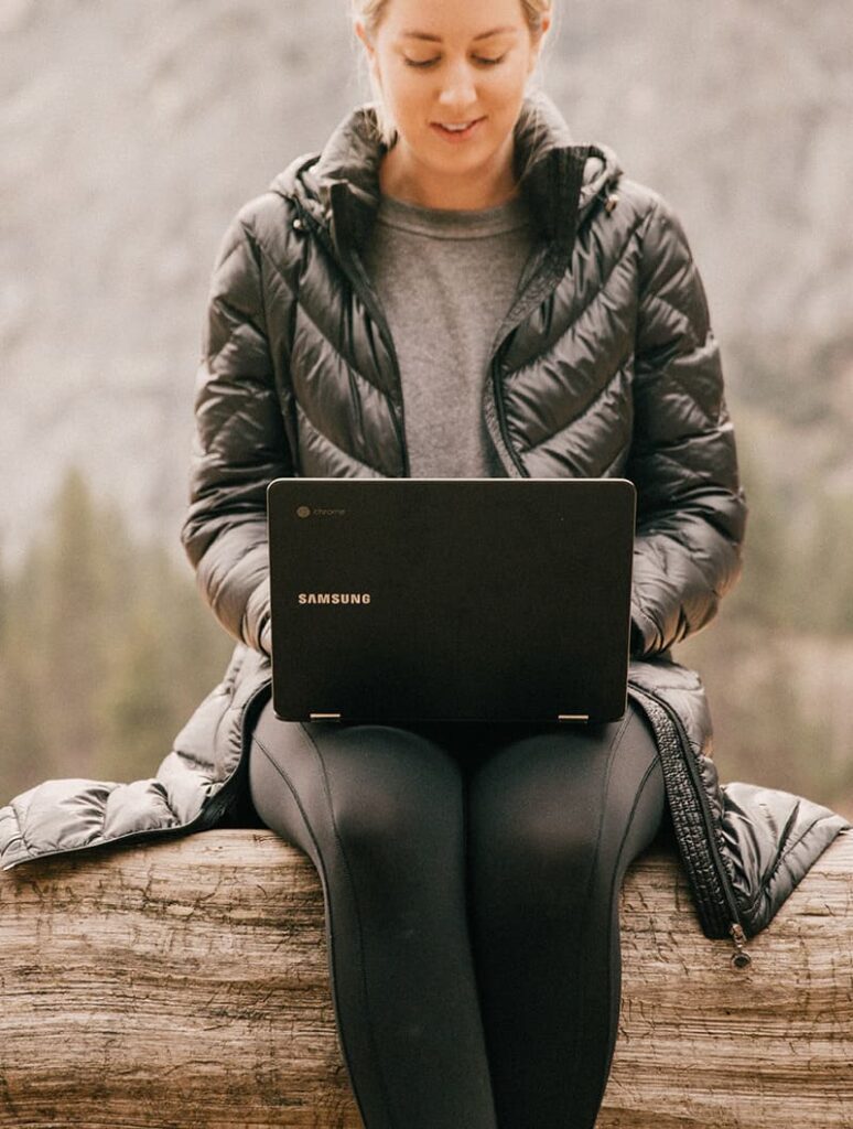 Woman sitting on log using laptop
